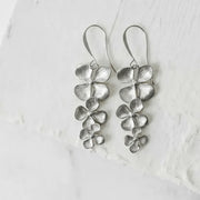 silver orchid earrings on white blurred background flat lay