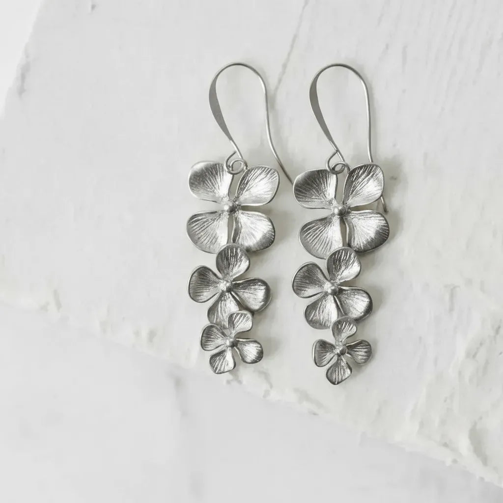 silver orchid earrings on white blurred background flat lay
