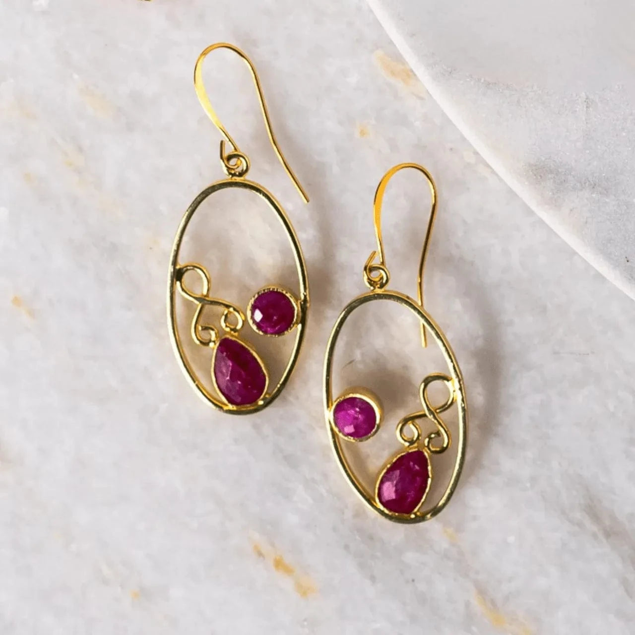 Gold earrings with red gemstones on a light background
