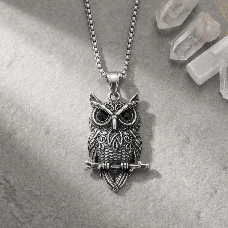 Silver owl pendant necklace on a textured surface with crystals in the background