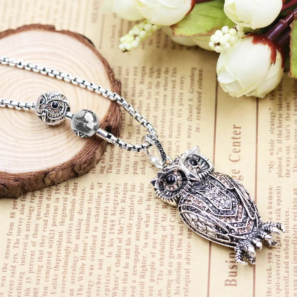 Silver owl pendant necklace on a textured surface with flowers