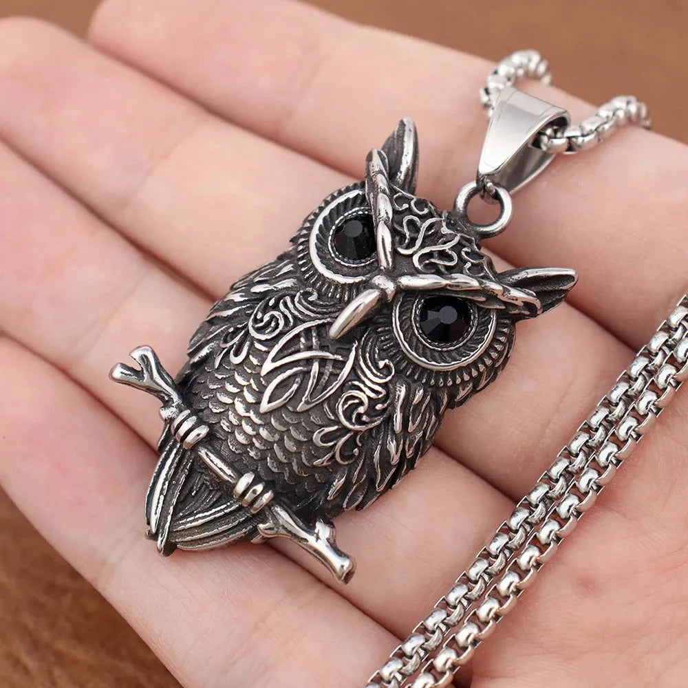 Silver owl pendant on a chain held in a hand against a brown background