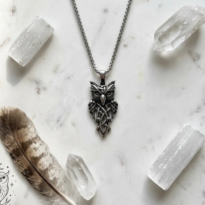 Silver owl pendant necklace on a marble surface with crystals and a feather.
