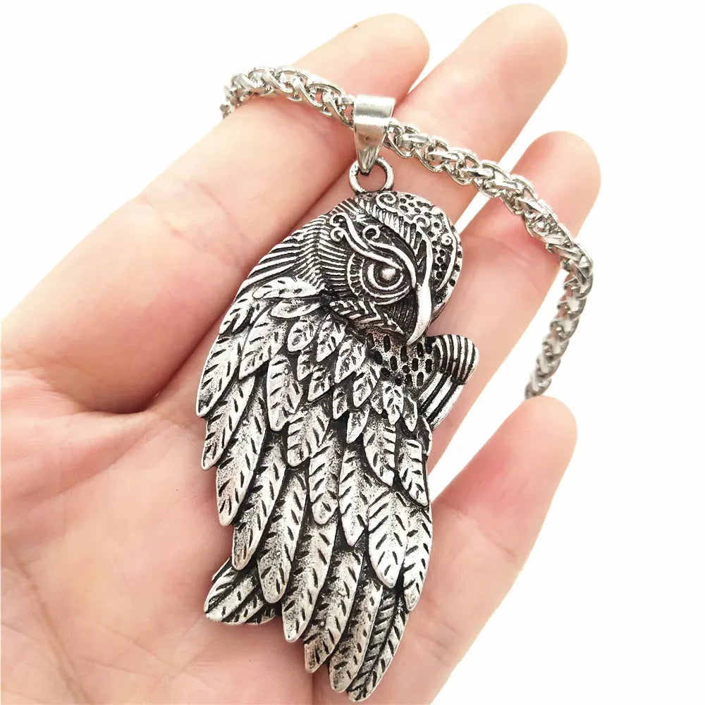 Silver wing-shaped pendant on a chain held in a hand against a white background