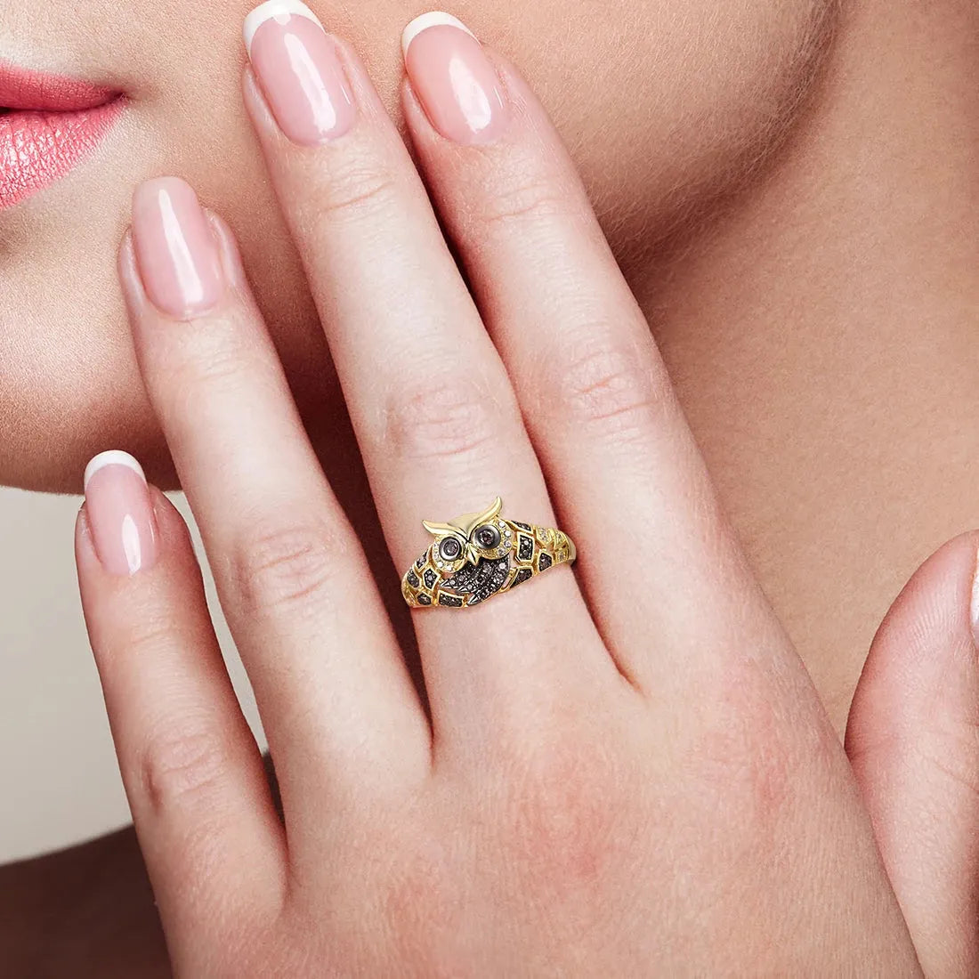 Gold ring with black gemstones on a woman's finger against a neutral background