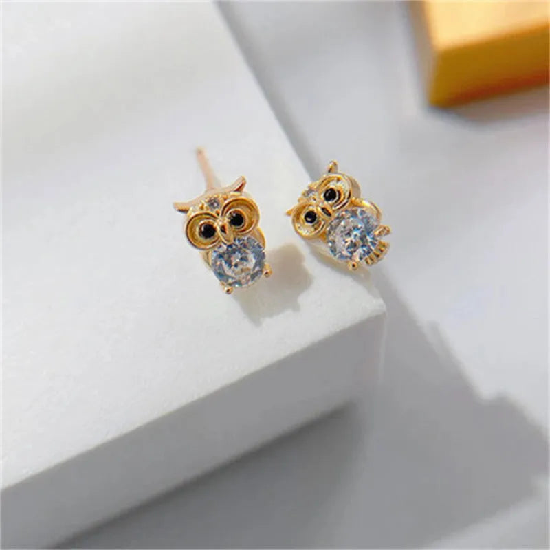 Gold owl-shaped earrings with gemstones on a white surface