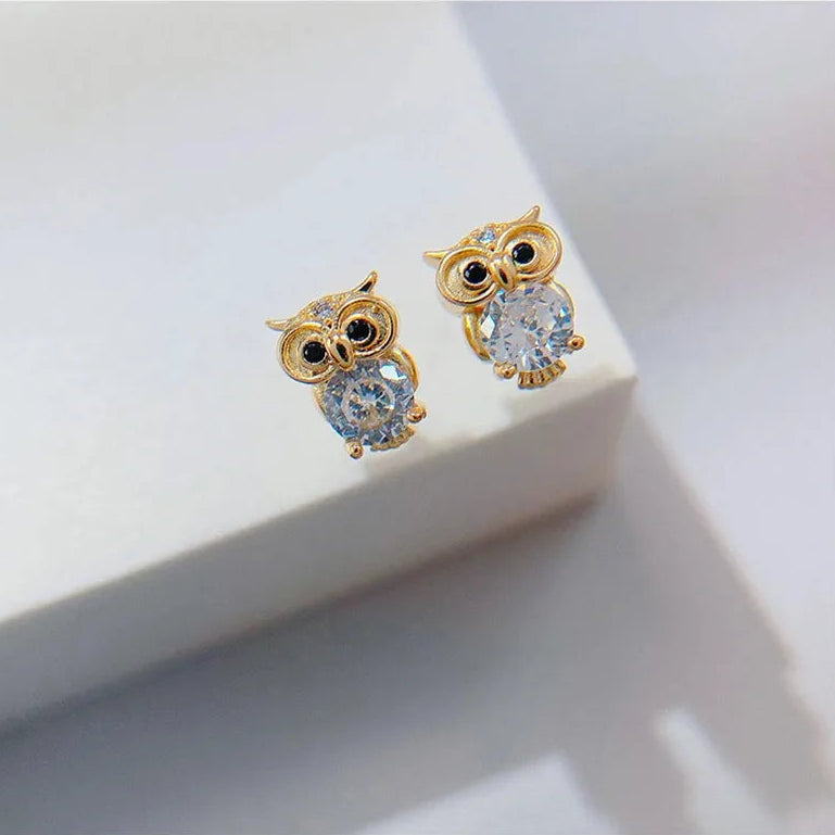 Gold owl-shaped earrings with gemstones on a white surface