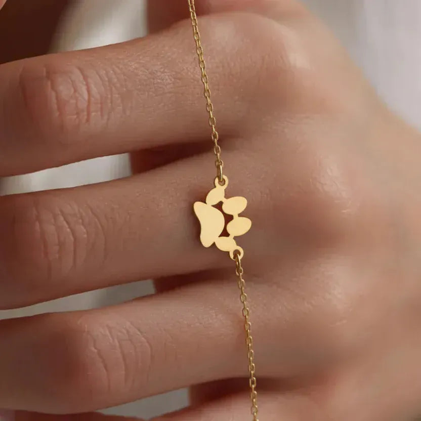 Gold bracelet with a heart-shaped charm held by a hand against a neutral background