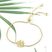 Gold bracelet with a paw charm on a white background with green leaves.