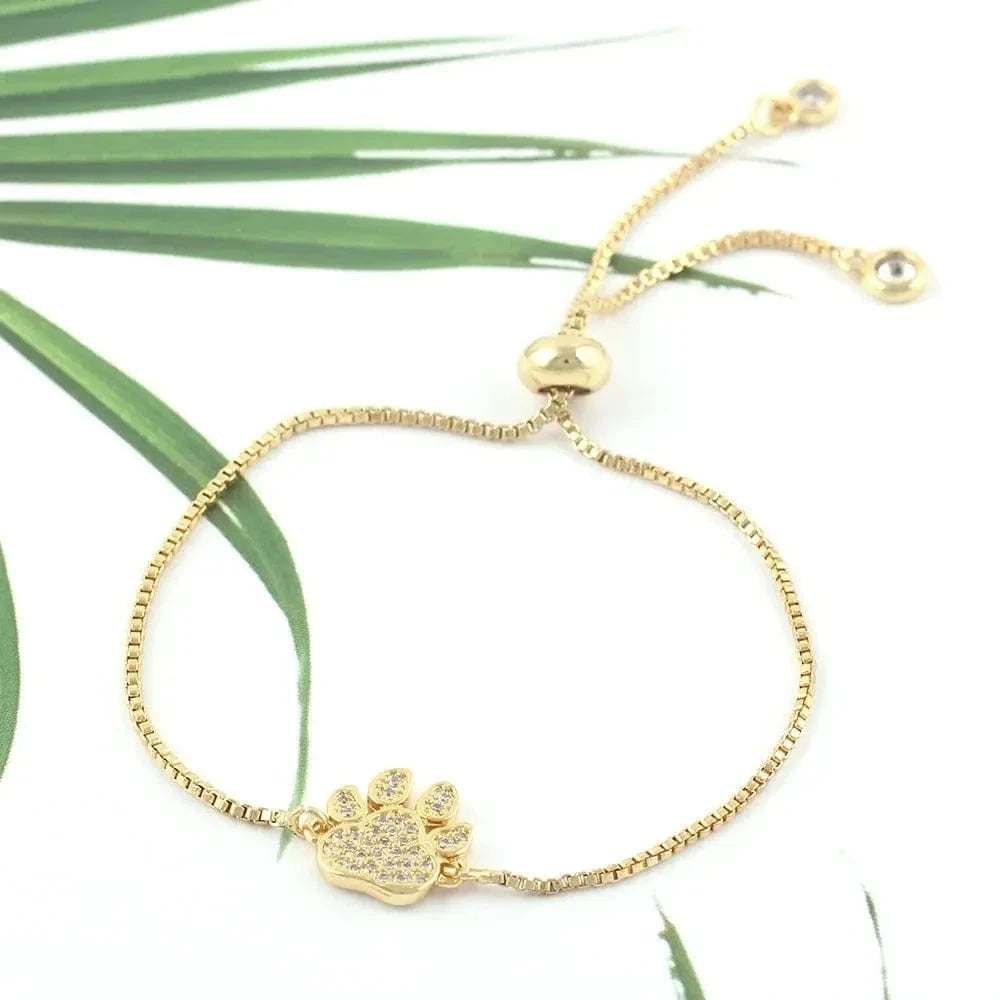 Gold bracelet with a paw charm on a white background with green leaves.