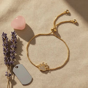 Gold bracelet with paw charm on a beige surface with lavender and a pink stone.
