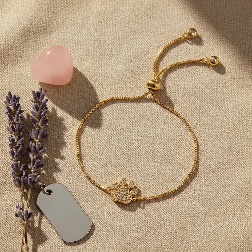 Gold bracelet with paw charm on a beige surface with lavender and a pink stone.