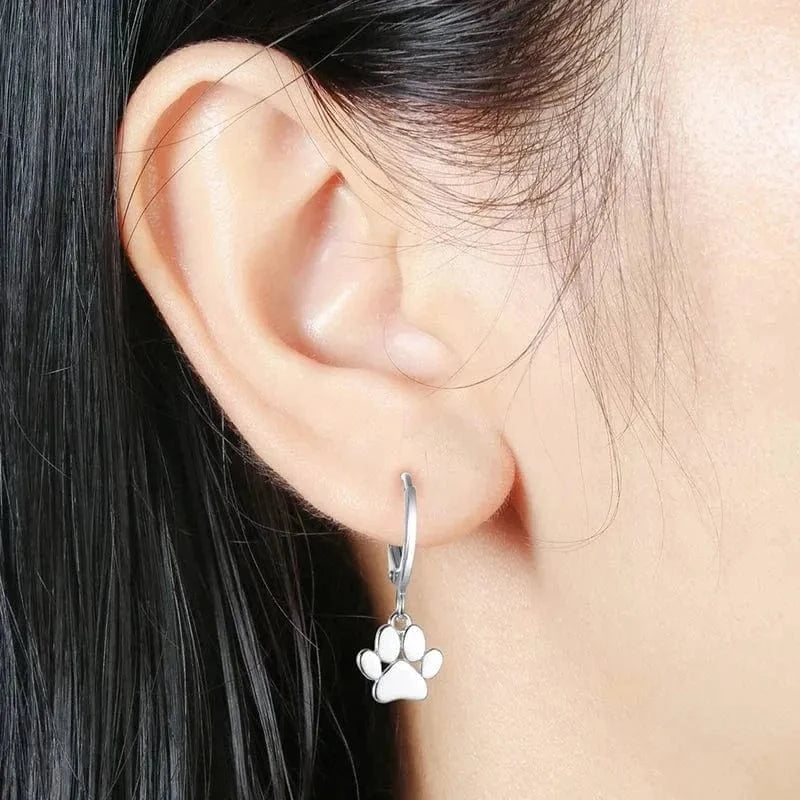 Silver hoop earring with a paw print charm worn by a person.
