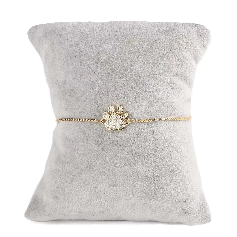 Gold bracelet with paw design on a gray cushion