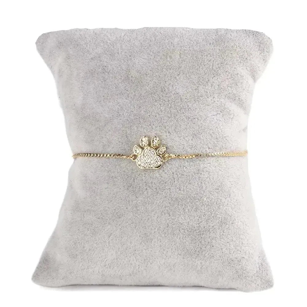 Gold bracelet with paw design on a gray cushion