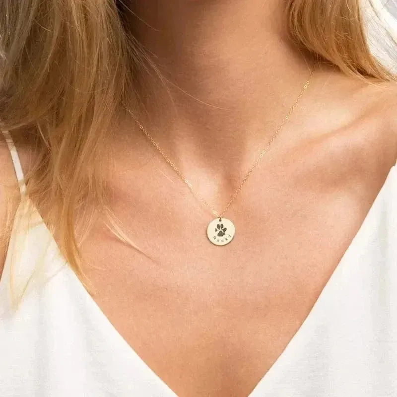 Gold necklace with a paw print pendant worn by a person in a white top.