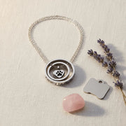 Necklace with paw print charm on a light surface with a pink stone and lavender.