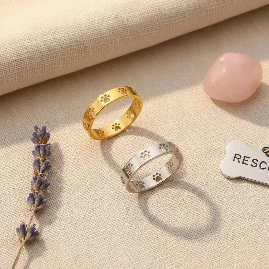 Gold and silver paw print rings on a beige background