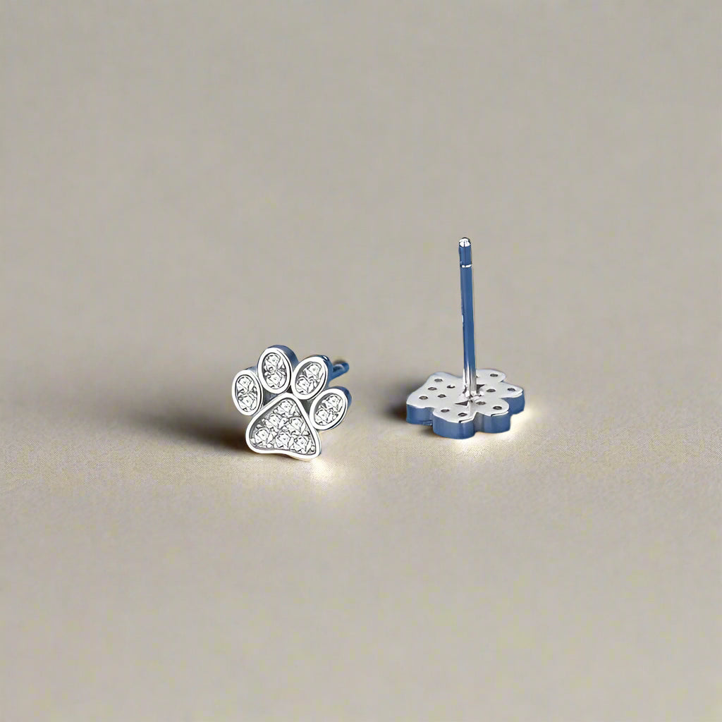 Silver paw print earrings on a blue fabric background