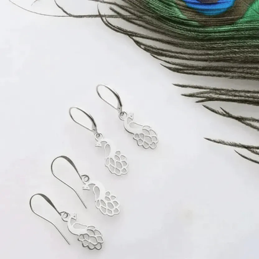 Silver earrings on a white surface with a peacock feather in the background