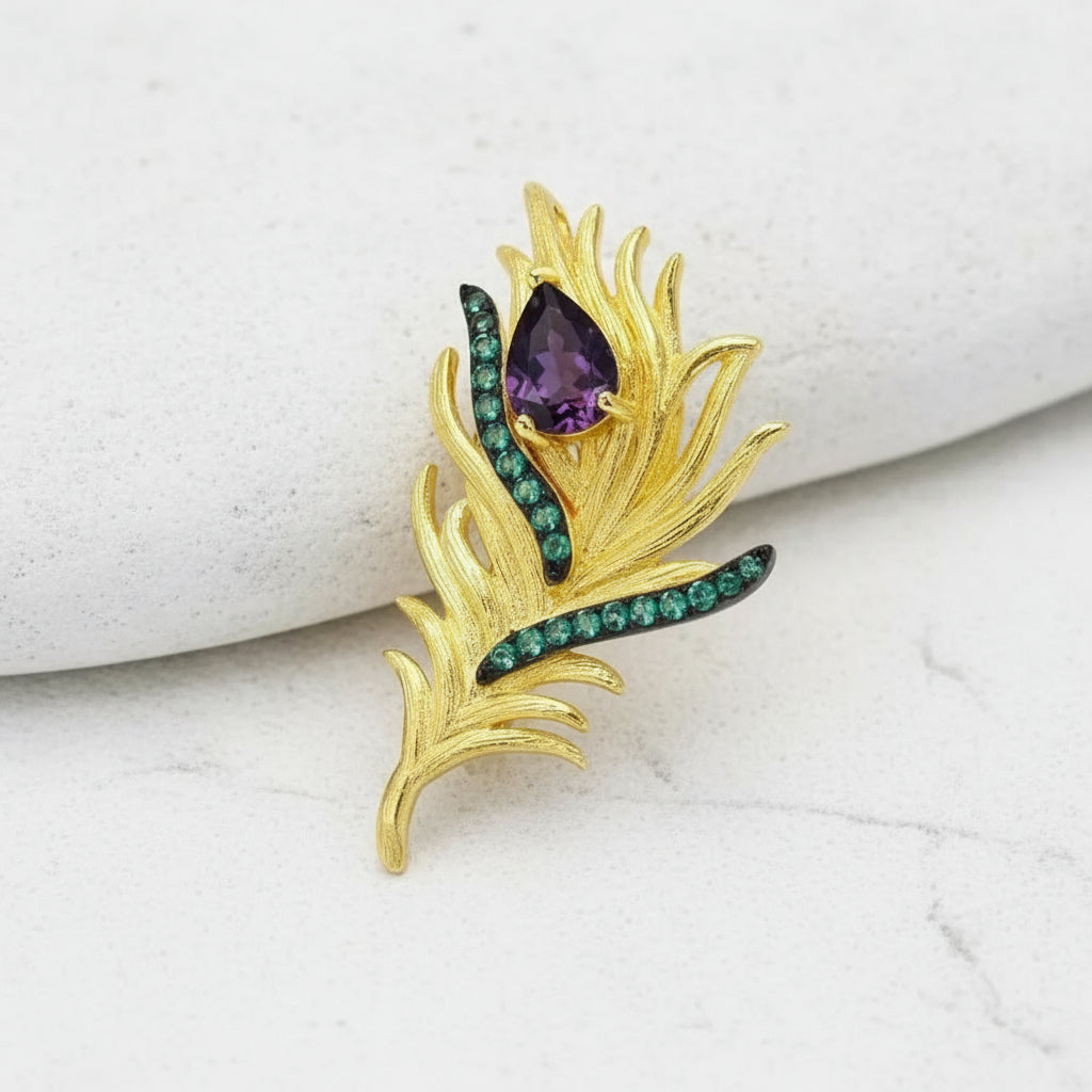 Gold brooch with purple and green gemstones on a white background