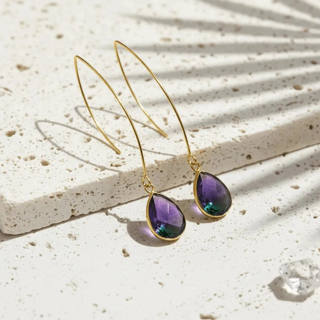 Gold earrings with purple gemstones on a textured surface