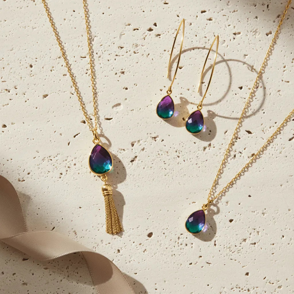 Jewelry set with gold necklaces and earrings featuring teardrop-shaped gemstones on a textured beige surface.