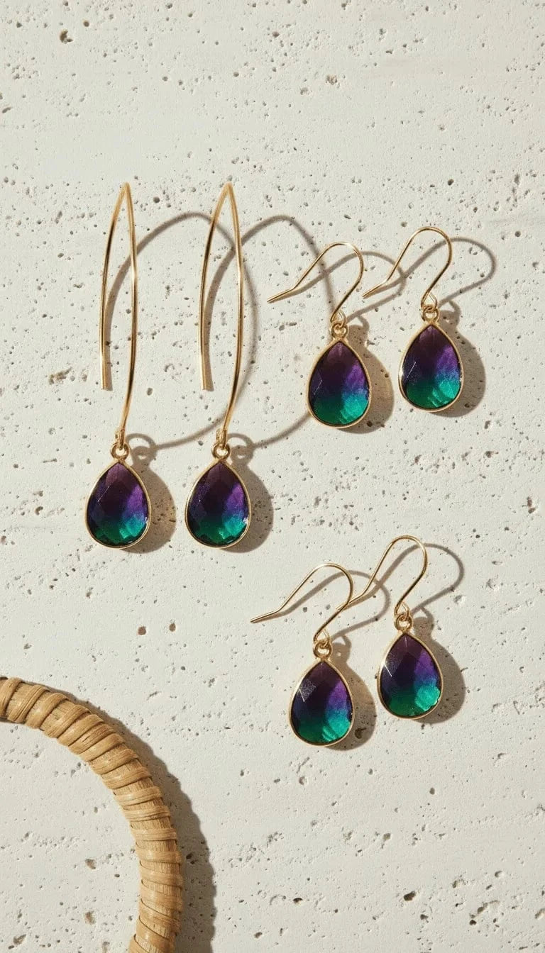 Teardrop-shaped earrings with iridescent finish on a textured beige surface