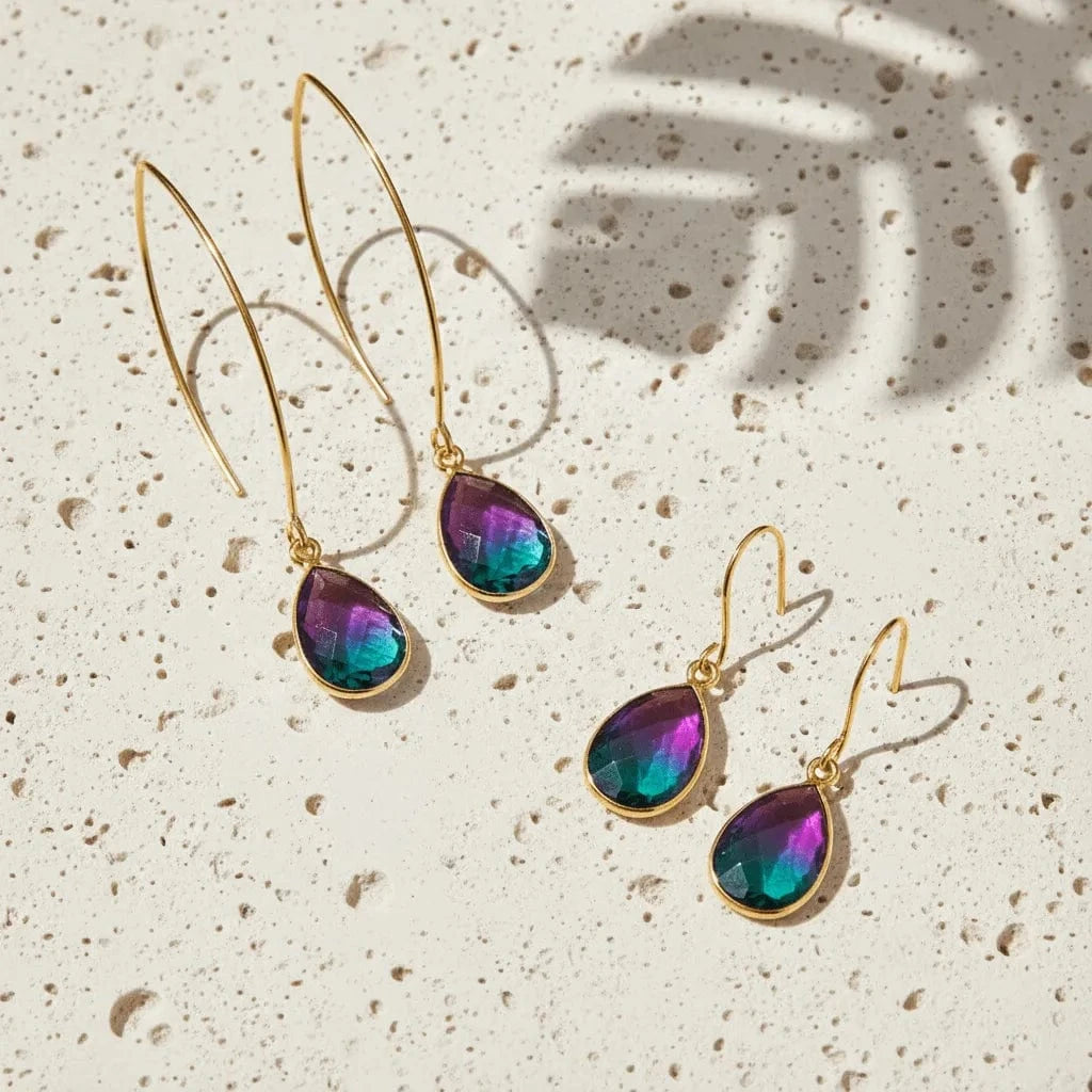 Gold earrings with colorful teardrop-shaped stones on a textured beige surface