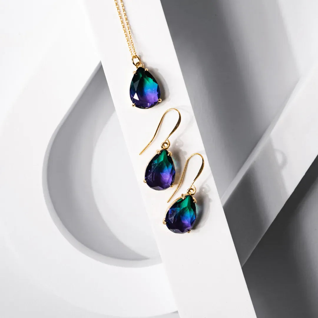 Teardrop-shaped earrings with gold settings on a white and gray background