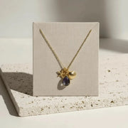 Gold necklace with a purple gemstone on a beige card, placed on a textured surface.