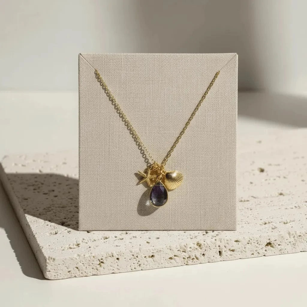 Gold necklace with a purple gemstone on a beige card, placed on a textured surface.