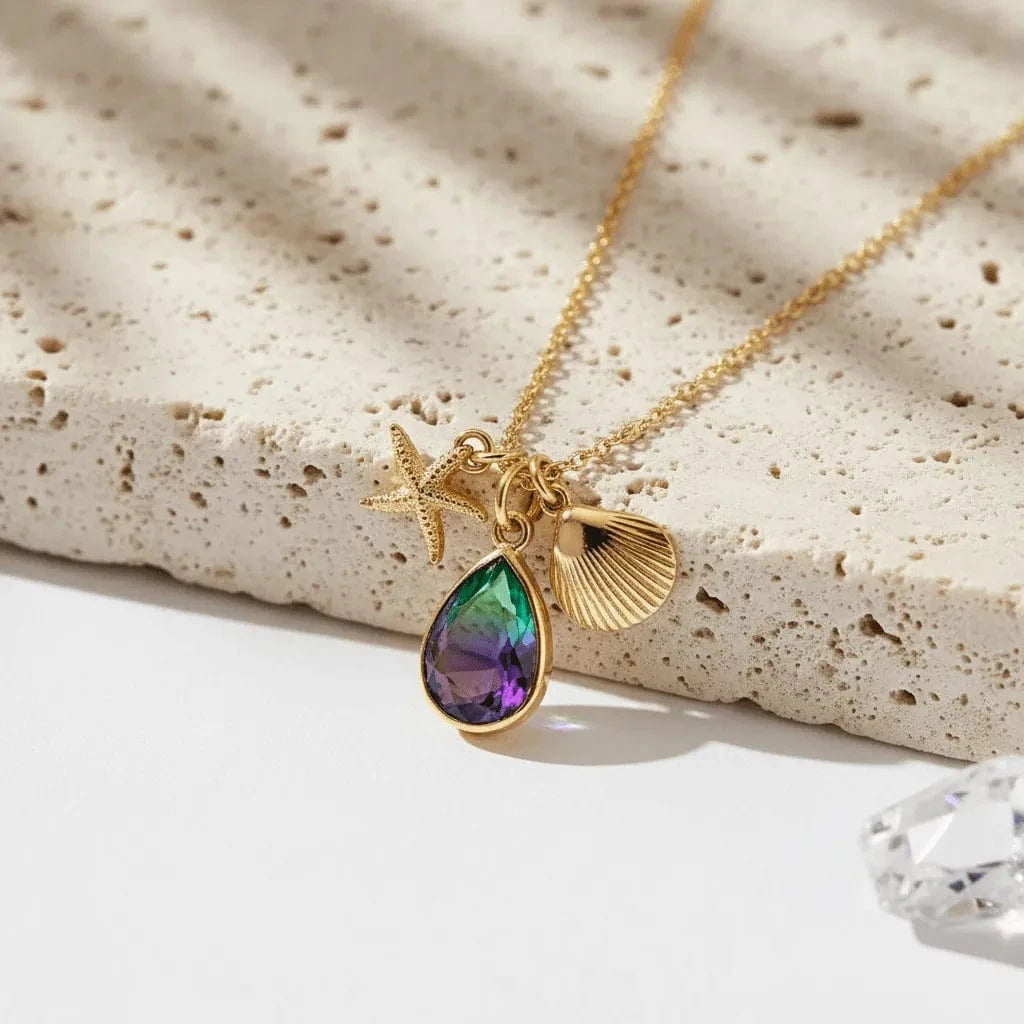 Gold necklace with a teardrop-shaped pendant and starfish charm on a textured surface