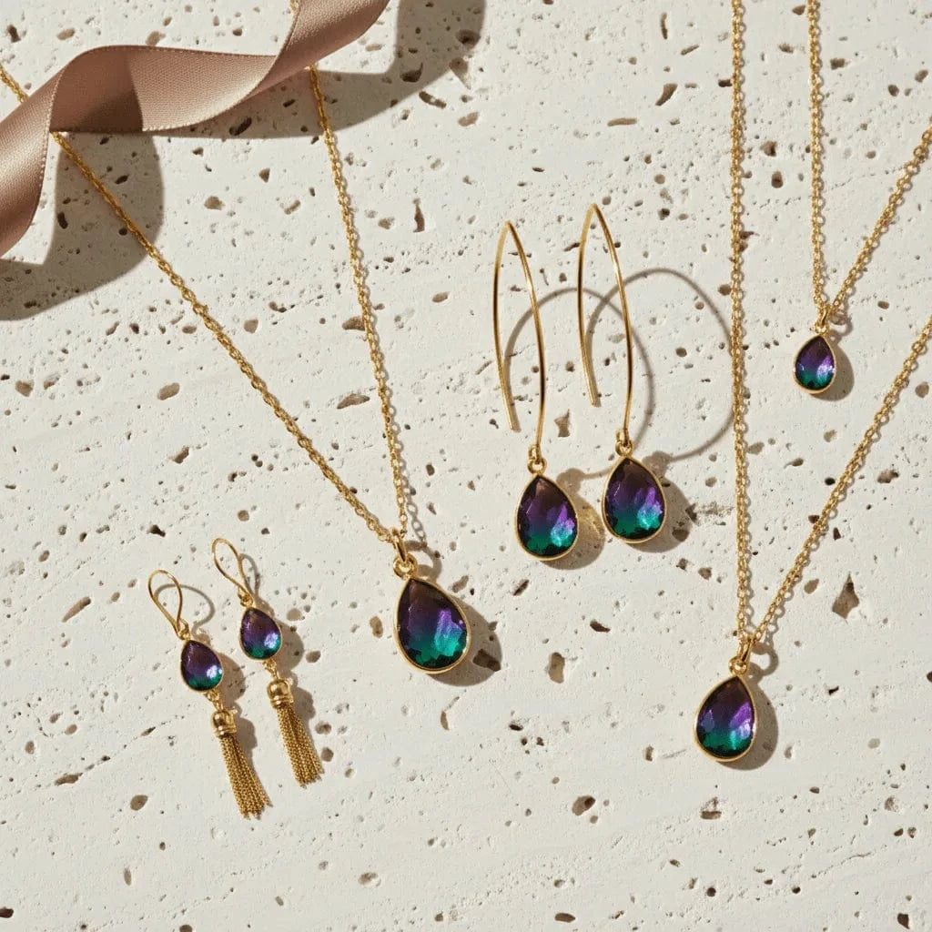 Gold jewelry set with teardrop-shaped gemstones on a textured beige surface