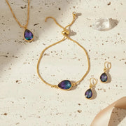 Gold jewelry set with purple stones on a textured beige surface