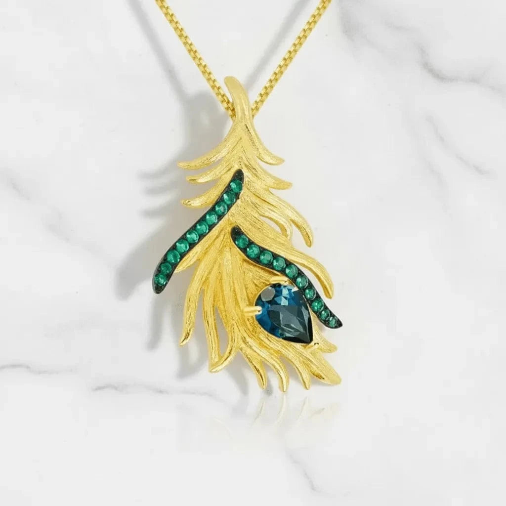 Gold feather-shaped pendant with green gemstones on a white background