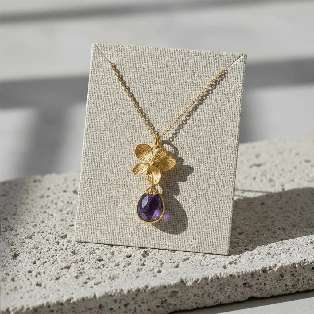 Gold necklace with a purple pendant on a display card against a neutral background