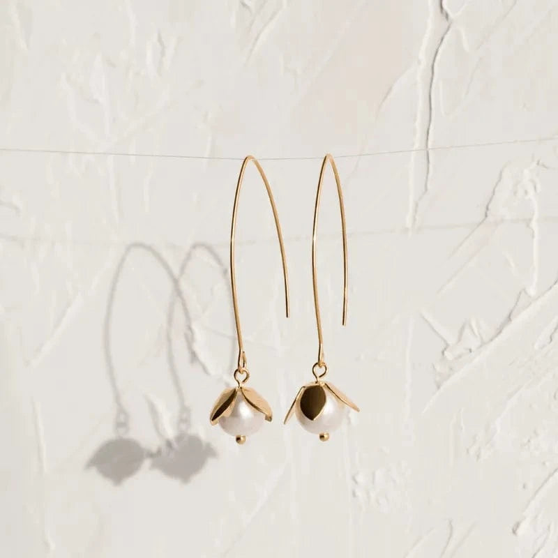 Gold earrings with pearl-like beads on a light gray textured background