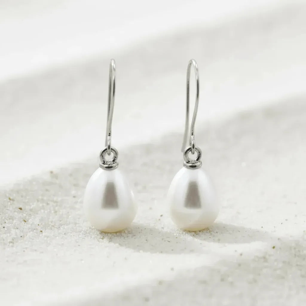 Pearl earrings on a white sandy background