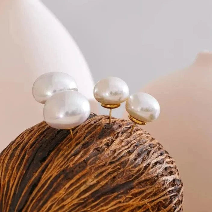 Pearl earrings on a textured brown surface with a white vase in the background