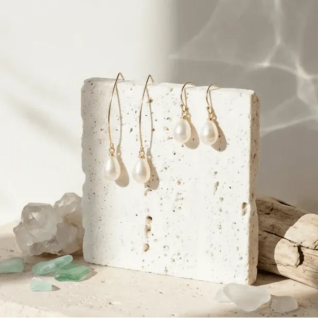 Pearl earrings on a textured white stand with natural elements in the background