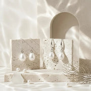 Pearl drop earrings displayed on a stone surface with text about their symbolism.