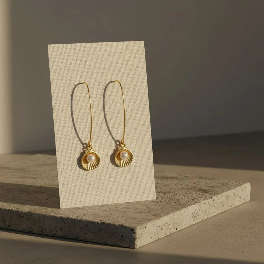Gold earrings with a pearl on a beige card against a neutral background