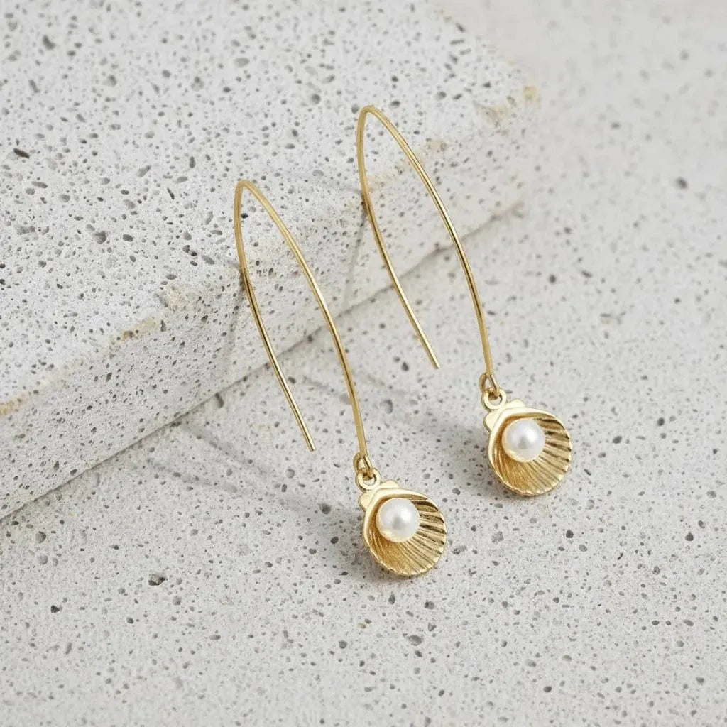 Gold earrings with pearl drops on a textured gray surface