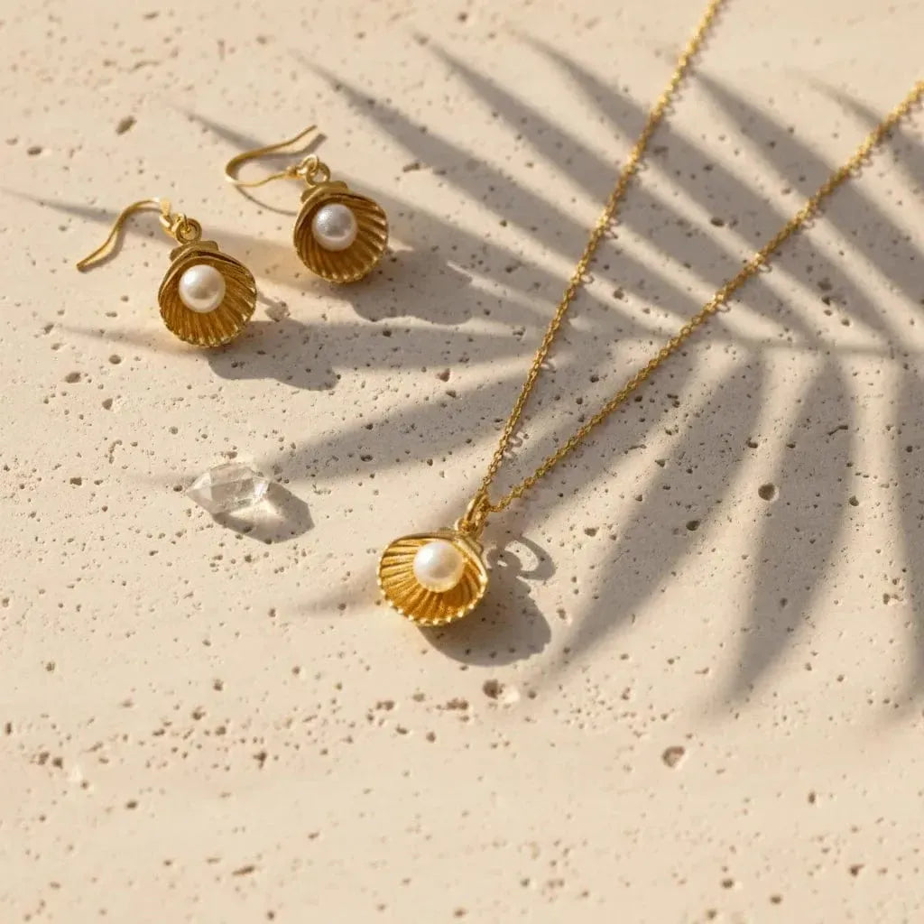 Gold jewelry set with shell and pearl design on a beige surface