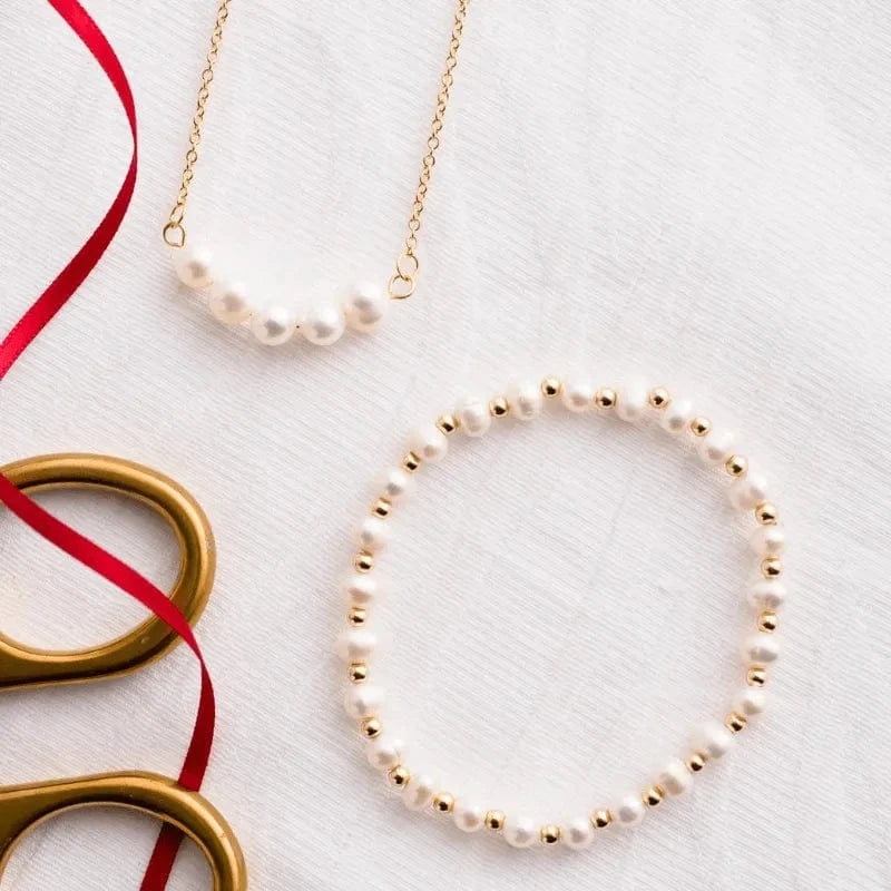 Pearl necklace and bracelet on a white background with gold scissors and red ribbon.