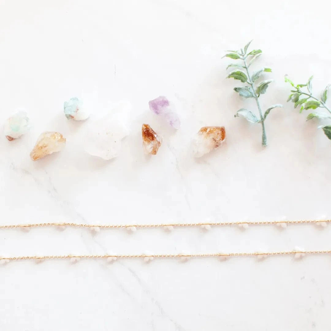 Gold necklace on a white surface with crystals and leaves