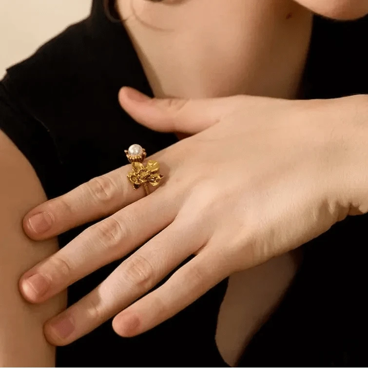 Close-up of a hand wearing a gold ring with a central stone, held against a neutral background.