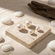 Pearl earrings on a stone surface with white stones and driftwood in the background