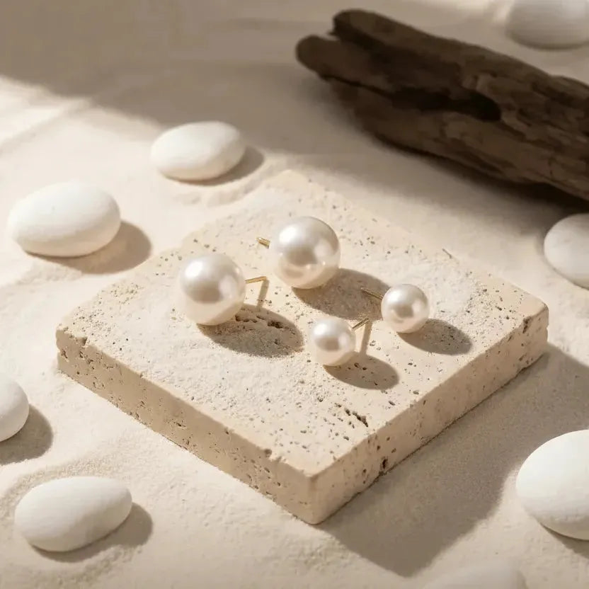 Pearl earrings on a stone surface with white stones and driftwood in the background